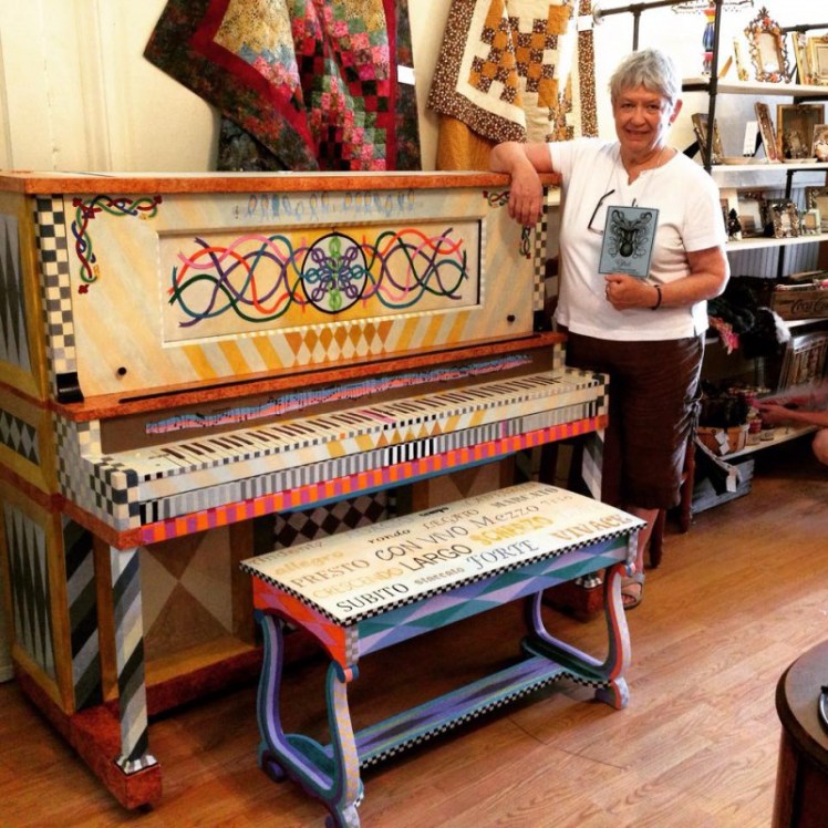 Artist Charleen Tyson stands with her finished work on the Painting the Piano Project.